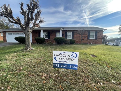 Brick house with a manicured lawn and a real estate sign in front.